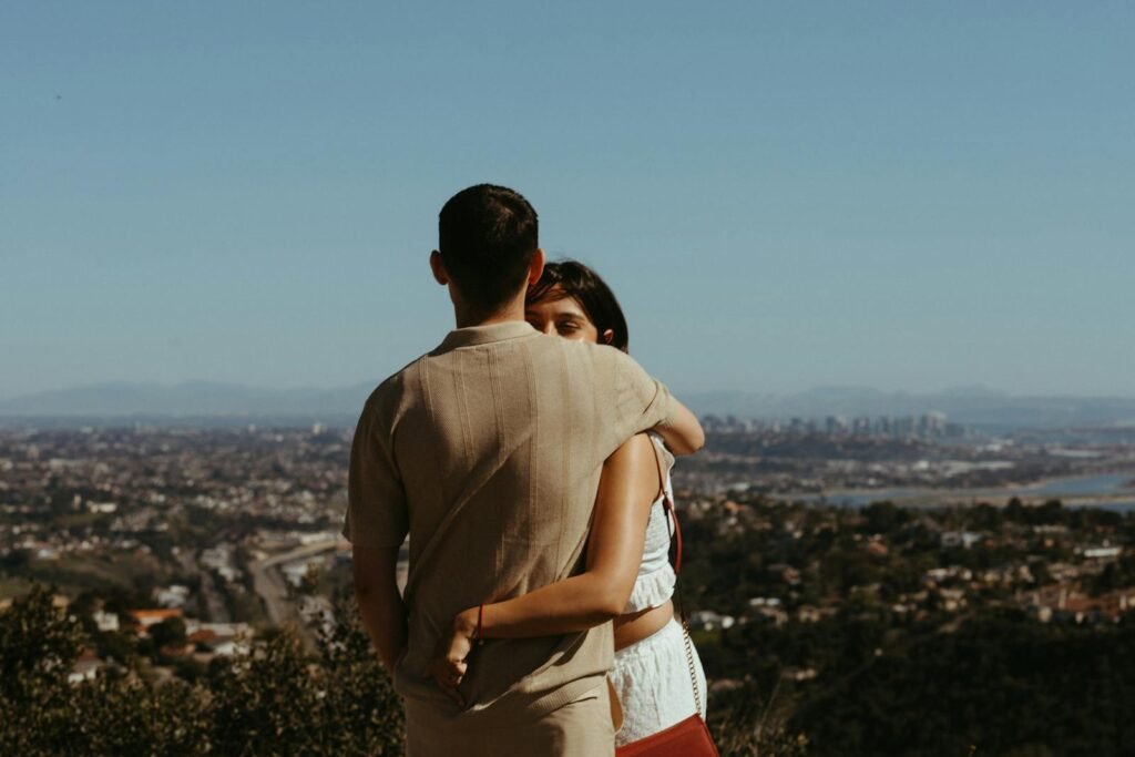 Young couple embracing with a scenic view of a city skyline in the background, captured on a sunny day.