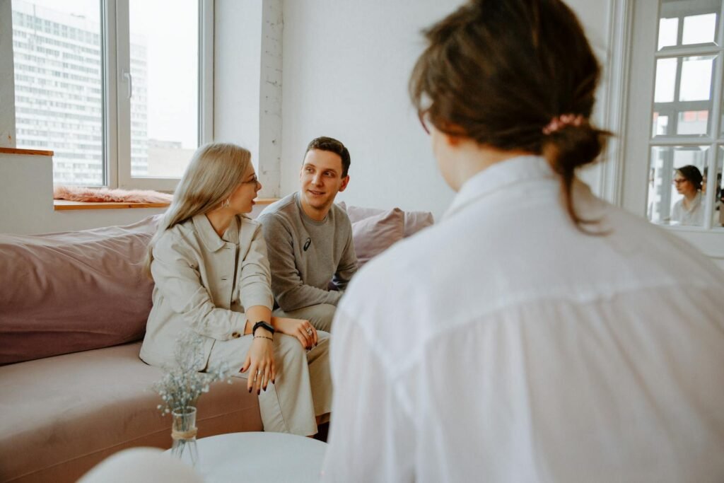 A couple engaged in a counseling session with a therapist in a modern indoor setting.